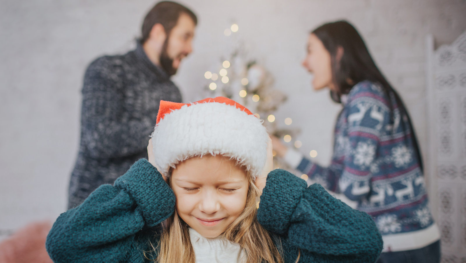 Kind hält sich die Ohren zu, während die Eltern im Hintergrund streiten