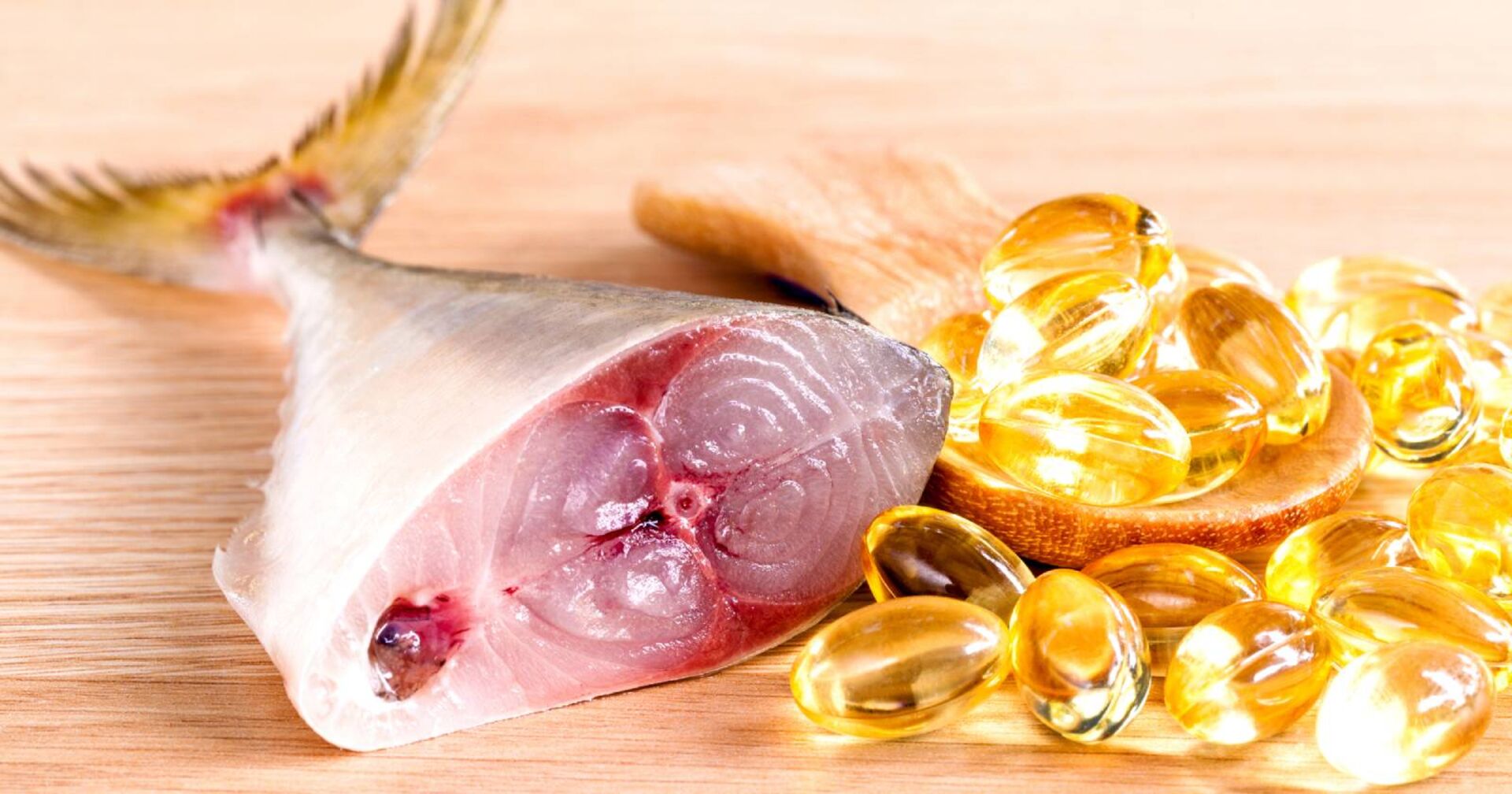 Die hintere Hälfte eines aufgeschnittenen rohen Fisches, die neben einer Handvoll Fischöl-Kapseln liegt