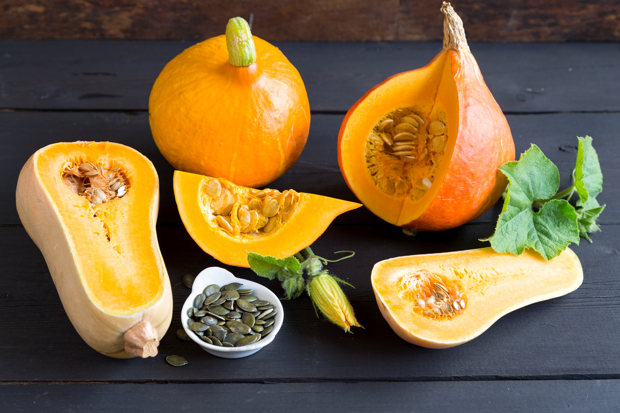 Drei aufgeschnittene Kürbisse sowie eine Schale mit Kürbiskernen, die auf einem Tisch stehen