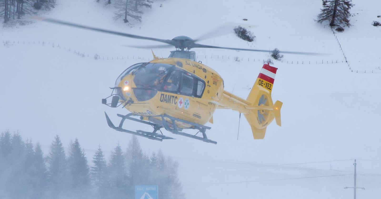 Gelber ÖAMTC-Rettungshubschrauber in einem Skigebiet.