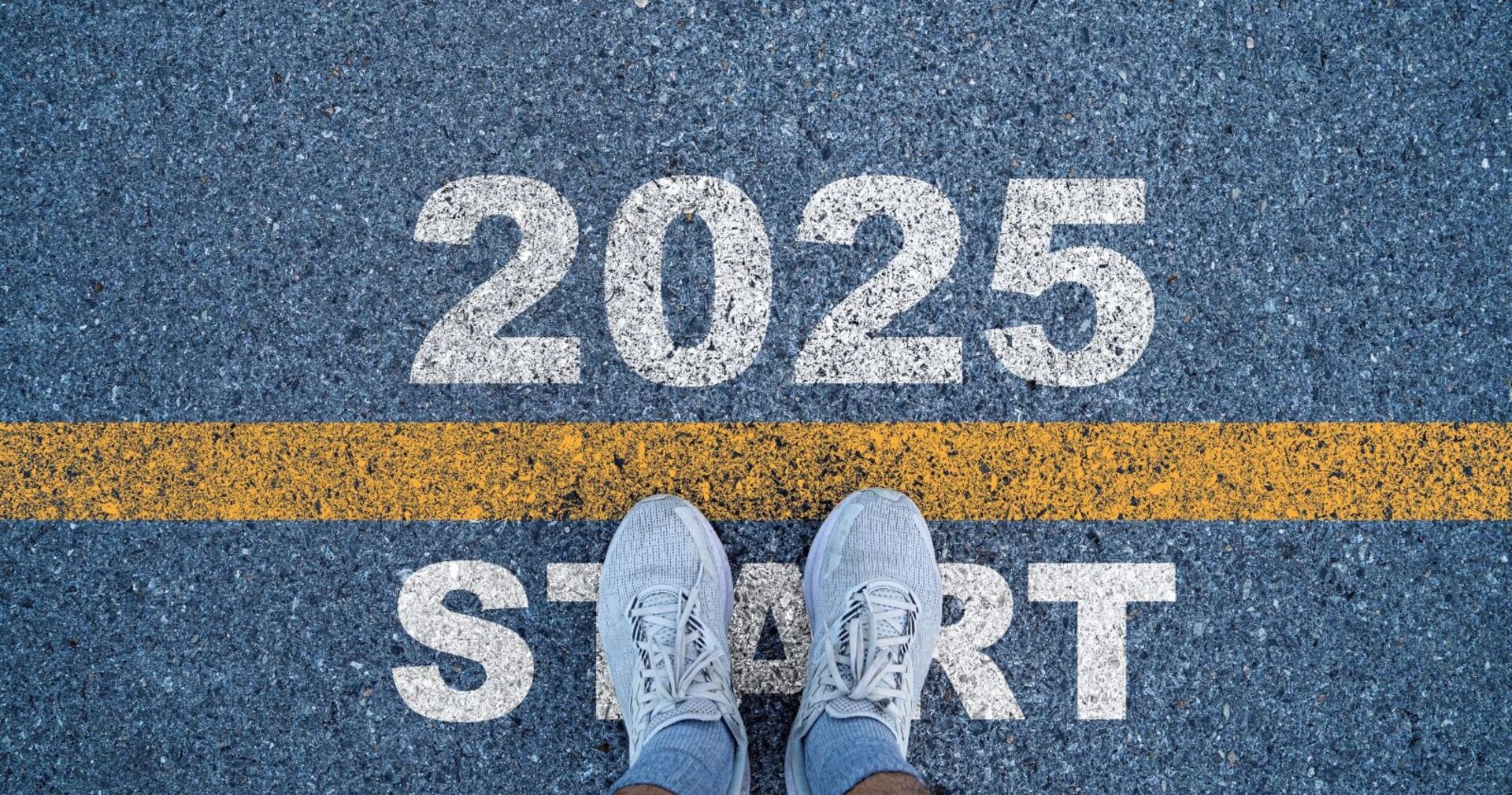 Schriftzug &quot;2025 Start&quot; und Sportschuhe auf einer Straße.