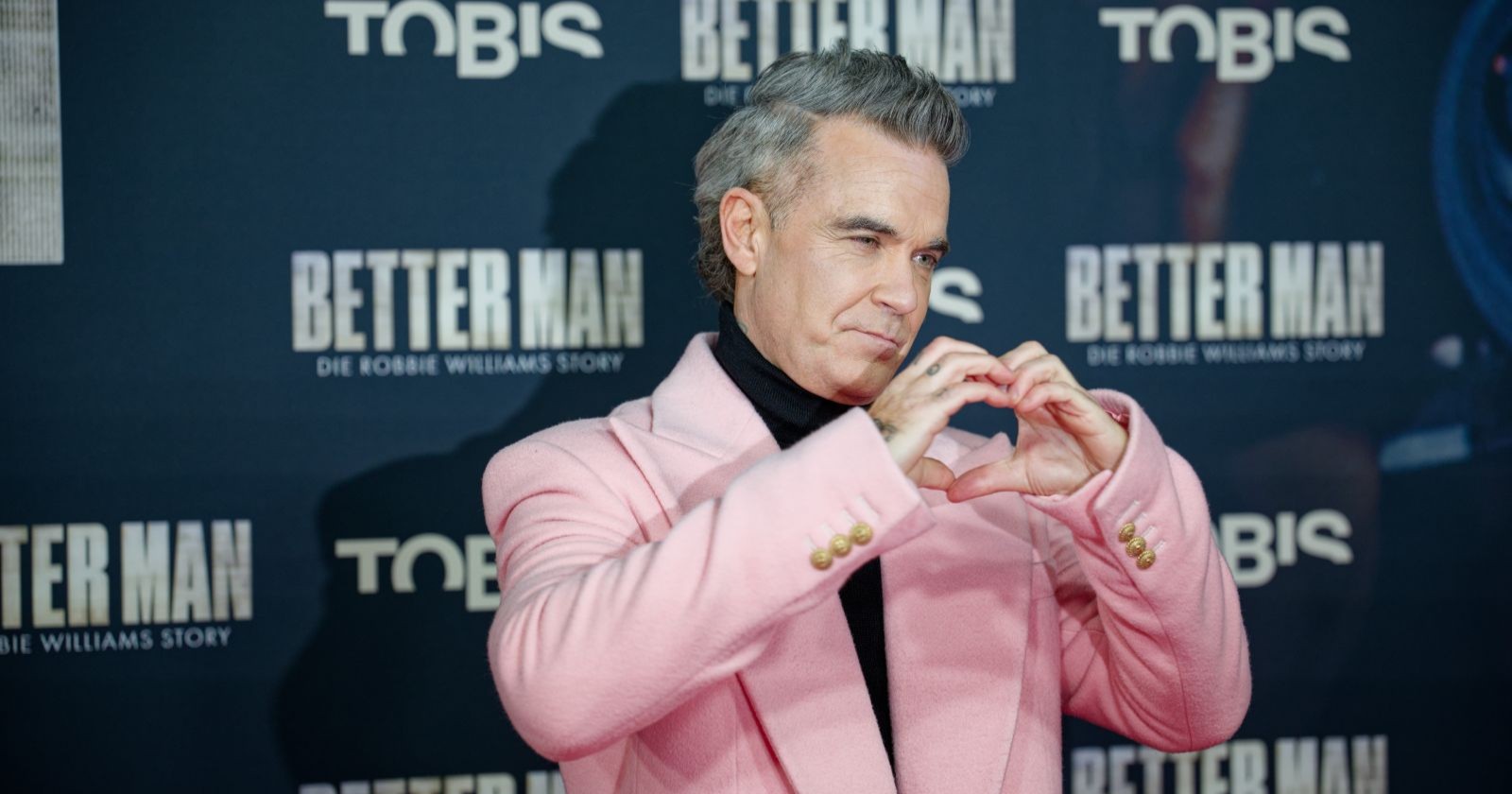 Robbie Williams formt ein Herz mit seinen Händen.