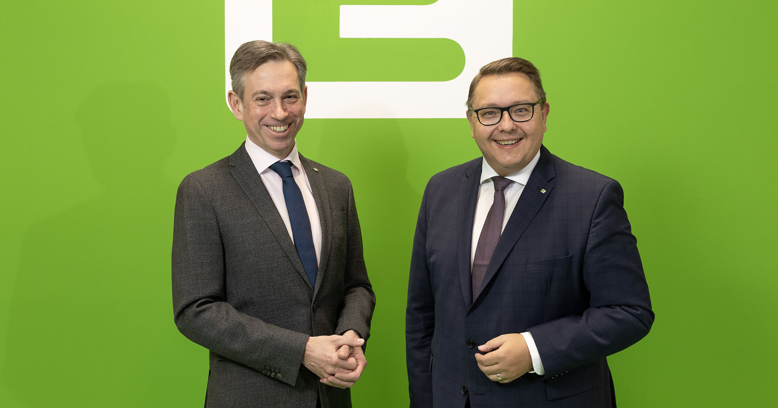 Zwei Männer in Anzügen stehen vor einer grünen Wand