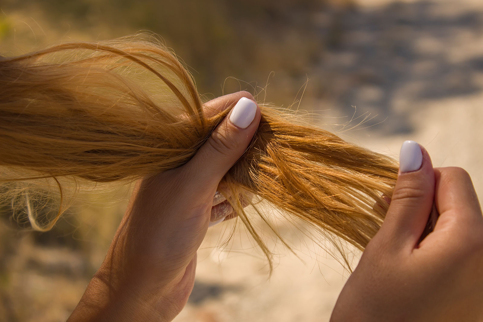 Frau testet ihre langen Haare auf strapazierte Spitzen | Credit: iStock.com/OleJohny