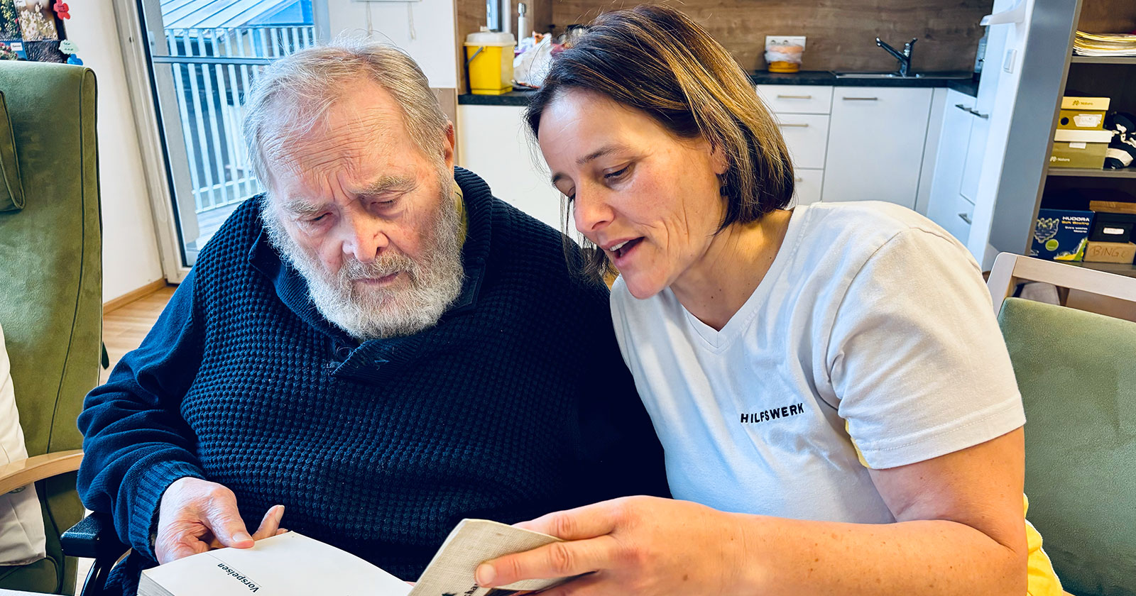 Weibliche Pflegekraft liest einem älteren Mann etwas vor | Credit: Hilfswerk Salzburg