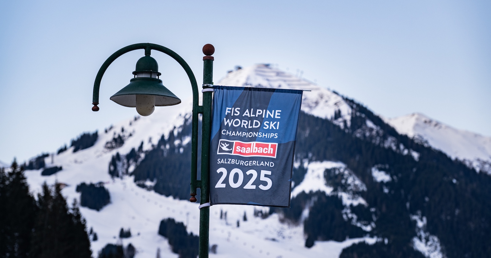 Die Ski-WM-Fahne hängt auf einer Laterne, dahinter der Berg.