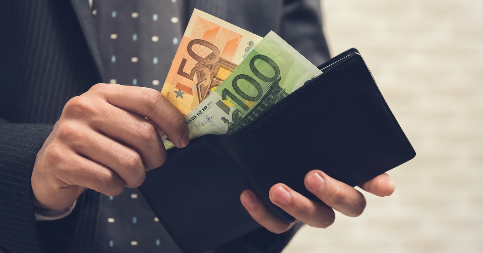 Ein Mann in Anzug holt Euroscheine aus seiner Geldtasche.