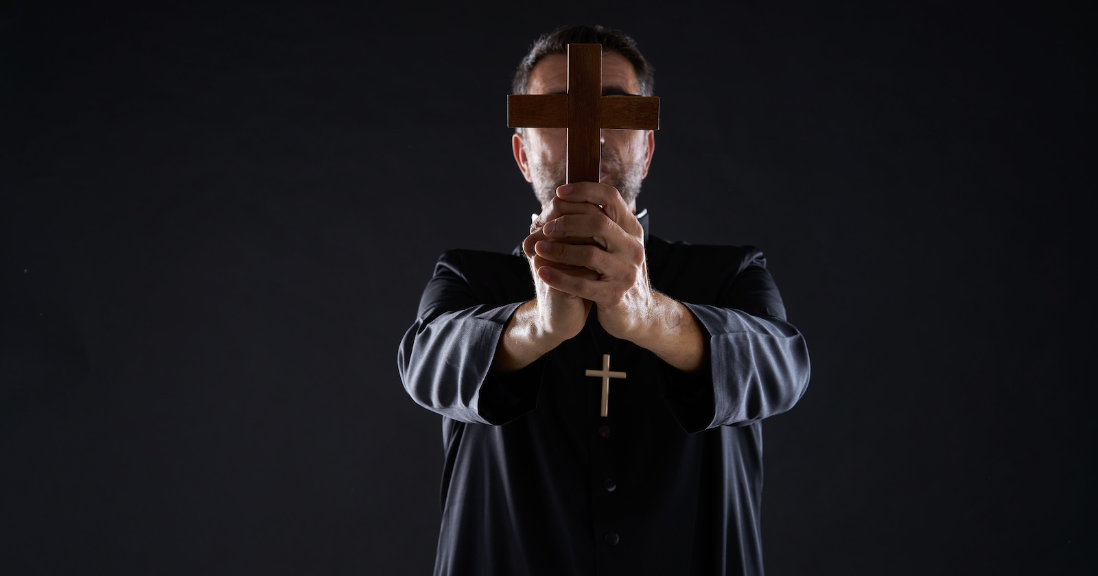 Ein Priester hält ein Kreuz vor sein Gesicht.