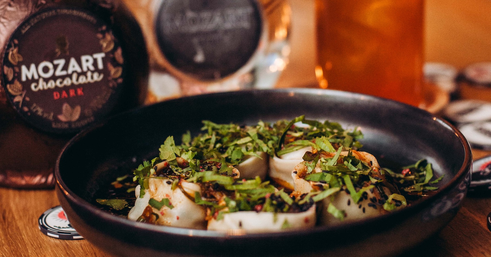 Küchengericht mit Kräutern im schwarzen Teller mit Likörflaschen und Cocktail-Glas