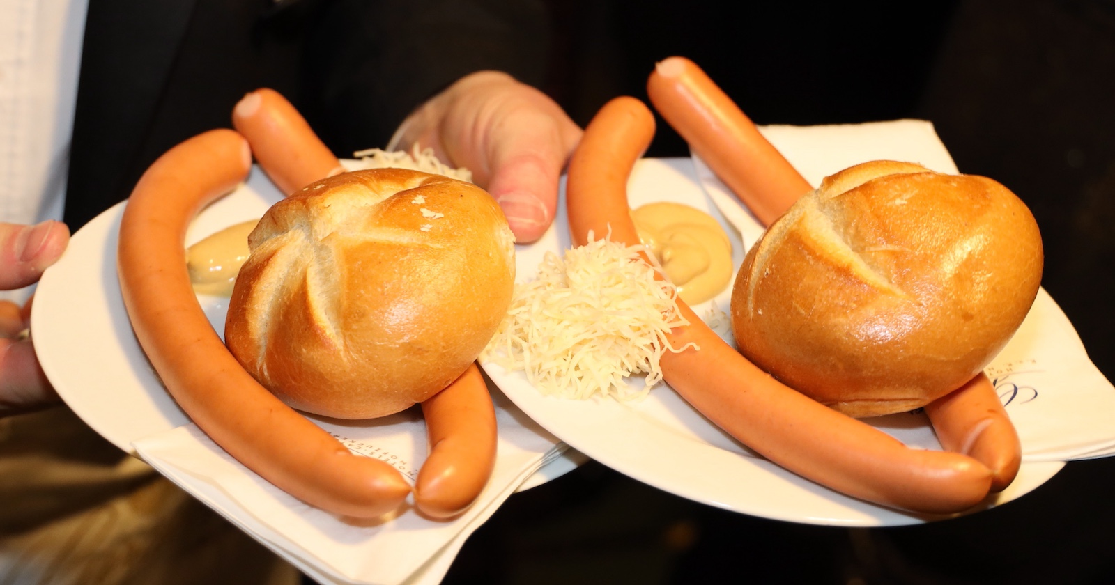 Ein Kellner serviert Würstel mit Senf und Kren auf weißen Tellern am Opernball