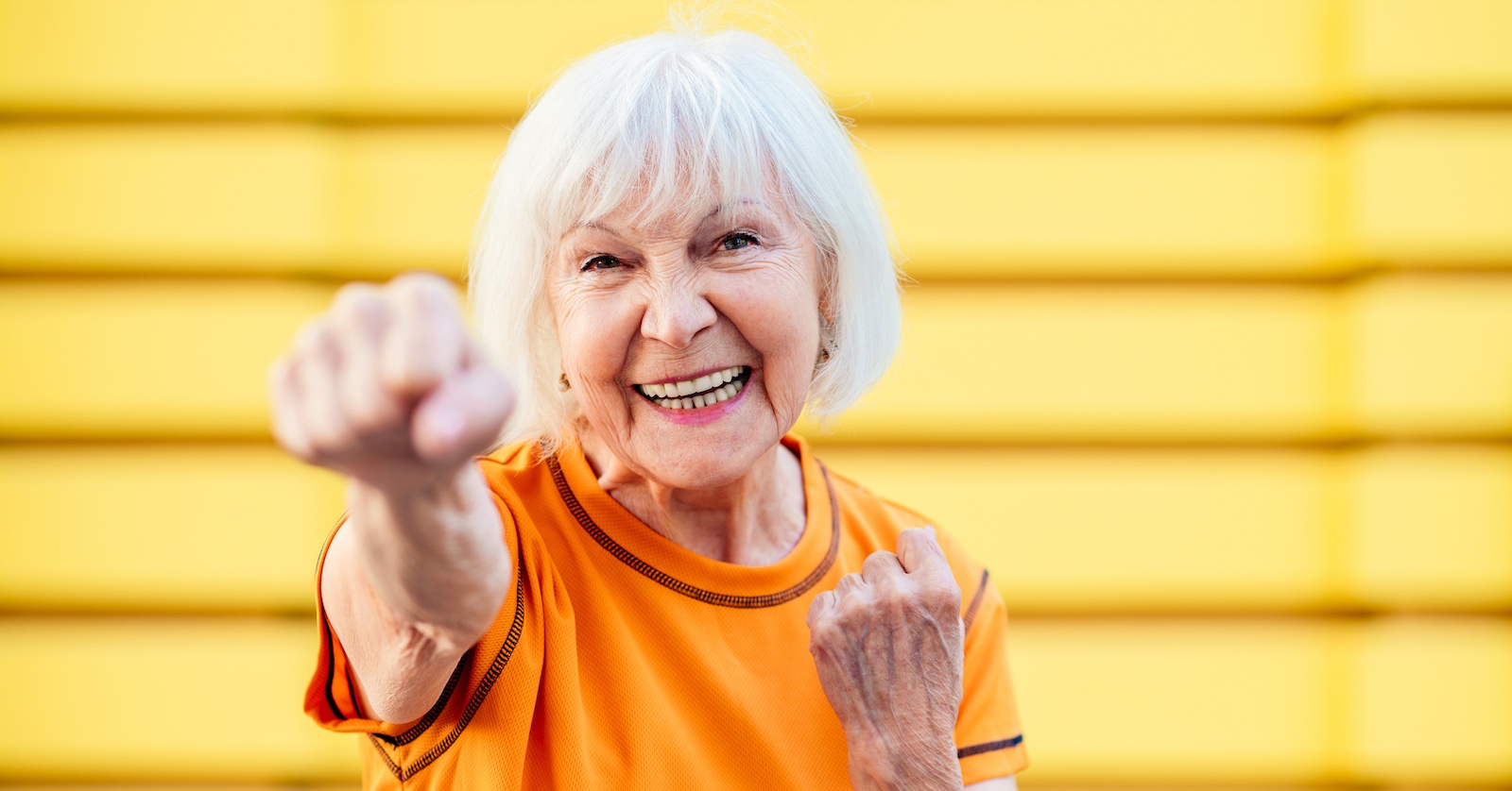 Eine weißhaarige Senioren hat Freude an der Bewegung; sie boxt beim Sport in die Luft.