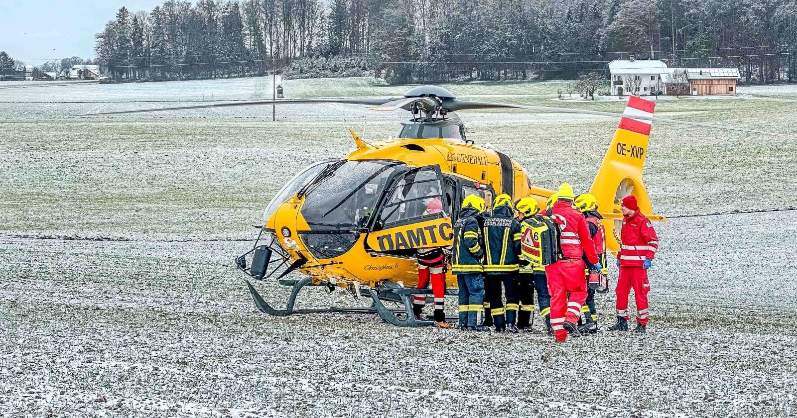Einsatzkräfte und ein gelber ÖAMTC-Hubschrauber auf einem Feld.