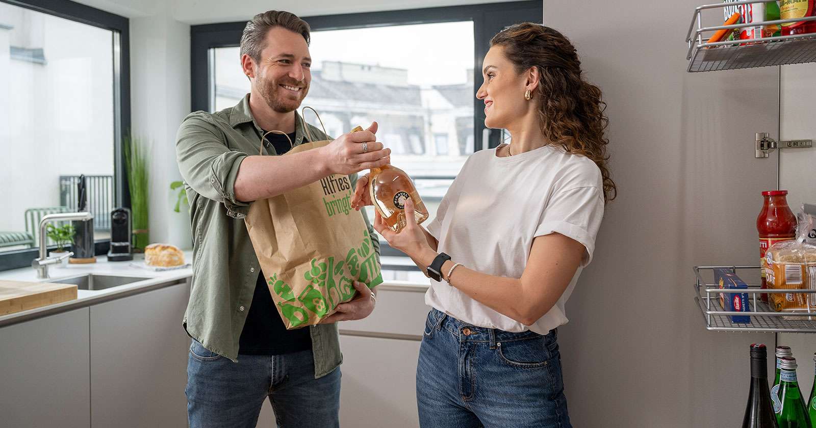 Junges Paar vor dem Kühlschrank mit der Einkaufstasche in der Hand | Credit: Alfies