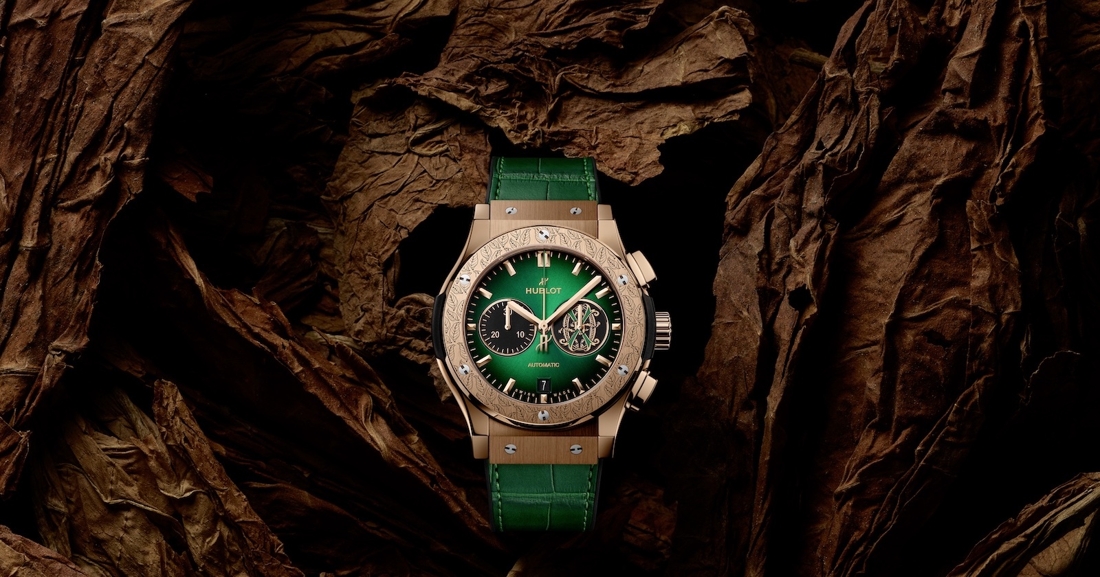 Goldene Uhr mit grünem Zifferblatt und grünem Armband vor braunem Hintergrund