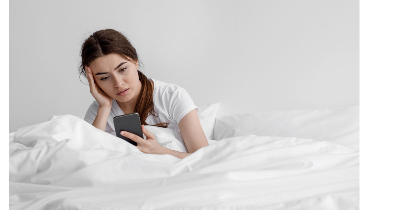 Junge Frau sitzt im Bett und schaut auf ihr Handy