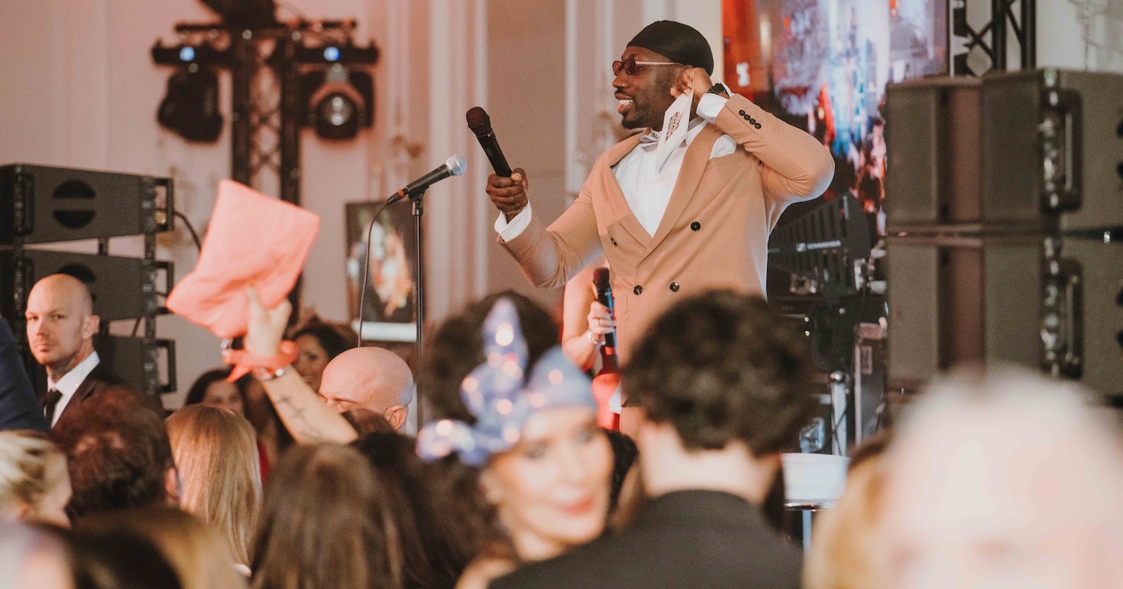 schwarzer HipHop-Musiker mit schwarzem Kopftuch, hellrosa Sako und Mikro auf der Bühne