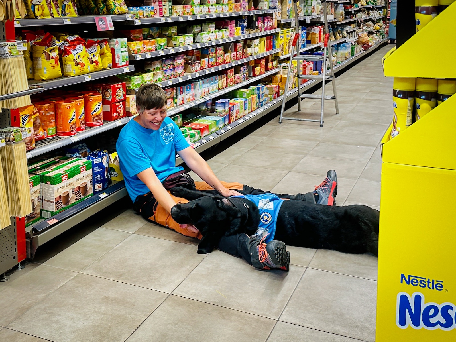 Eine Trainerin mit einem Assistenzhund in einem Supermarkt.