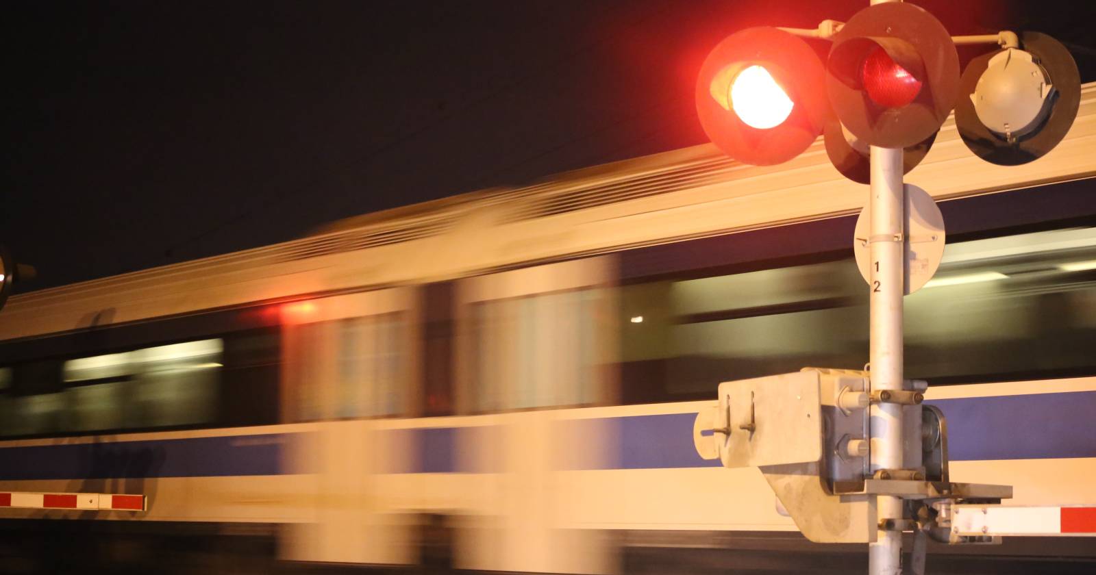 Ein verschwommen erscheinender Zug, der rasant eine Eisenbahnkreuzung überquert, während die Signalanlage rot leuchtet