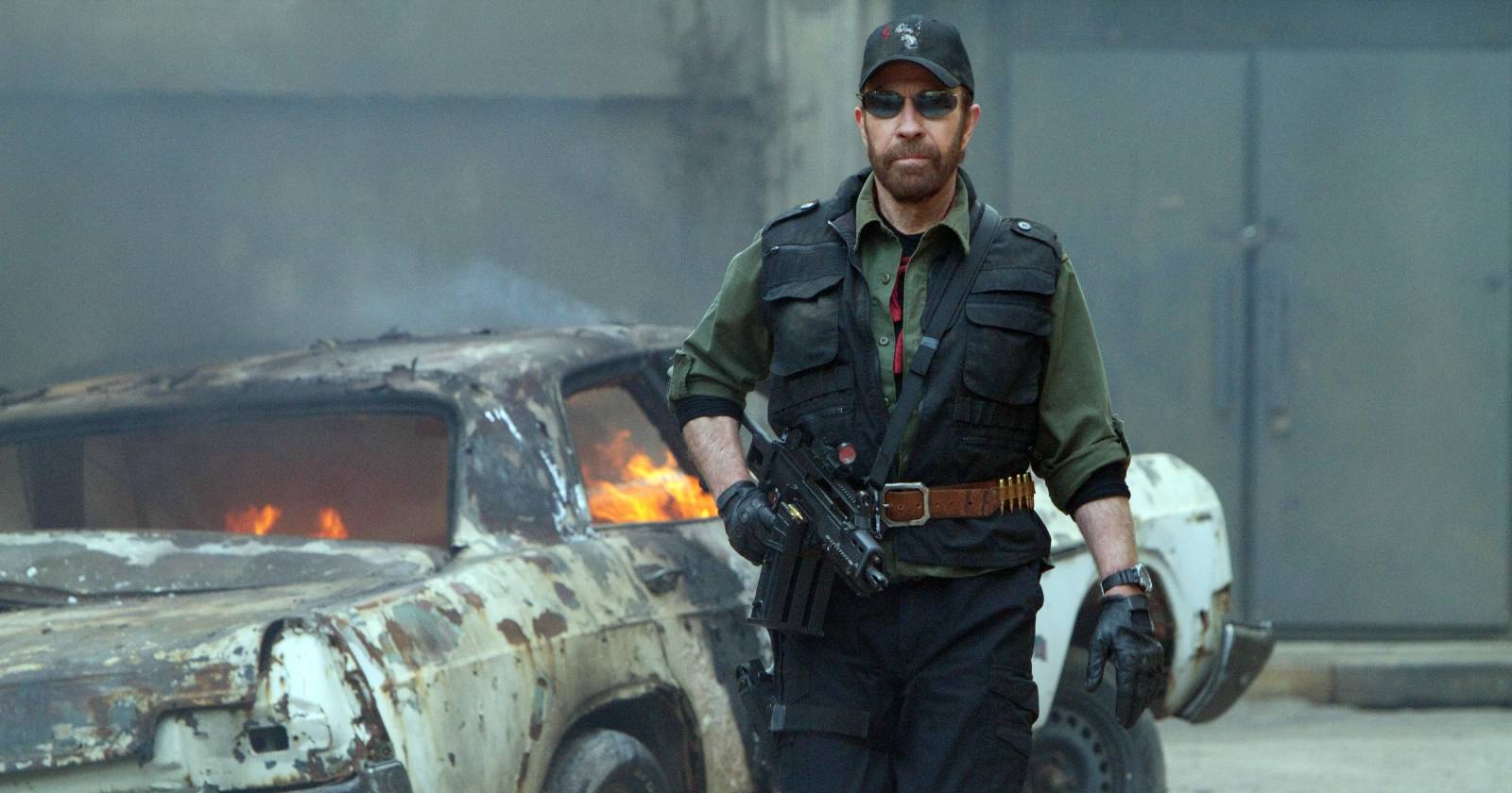 Eine Szene aus &quot;The Expandables 2&quot;, in der Chuck Norris mit einer Maschinenpistole in der Hand neben einem brennenden Auto steht