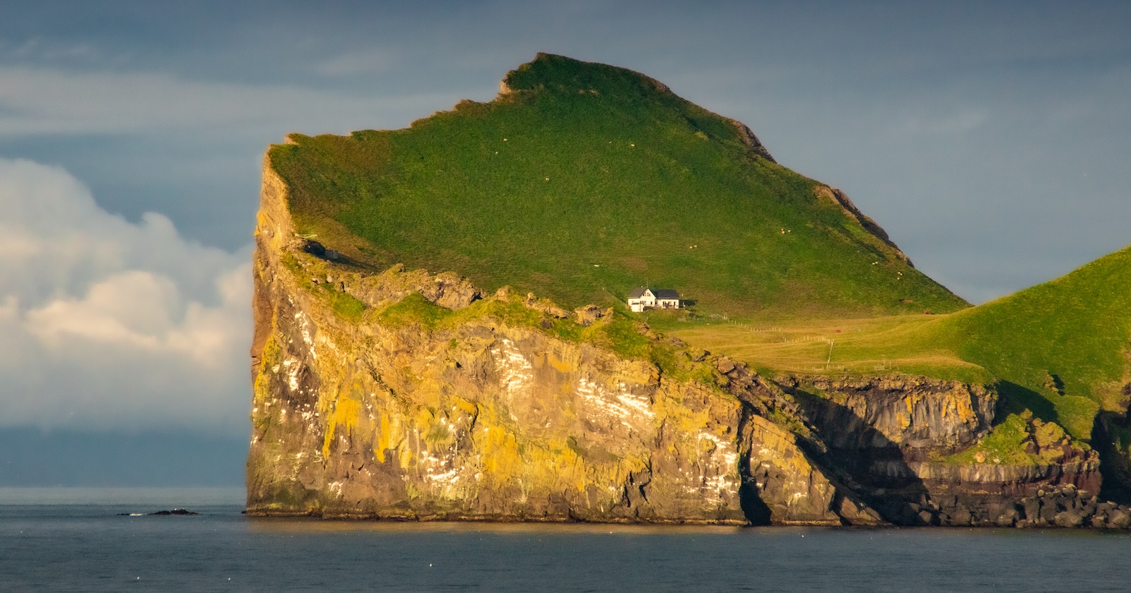 Haus auf einer Klippe einer wiesengrünen isländischen Insel