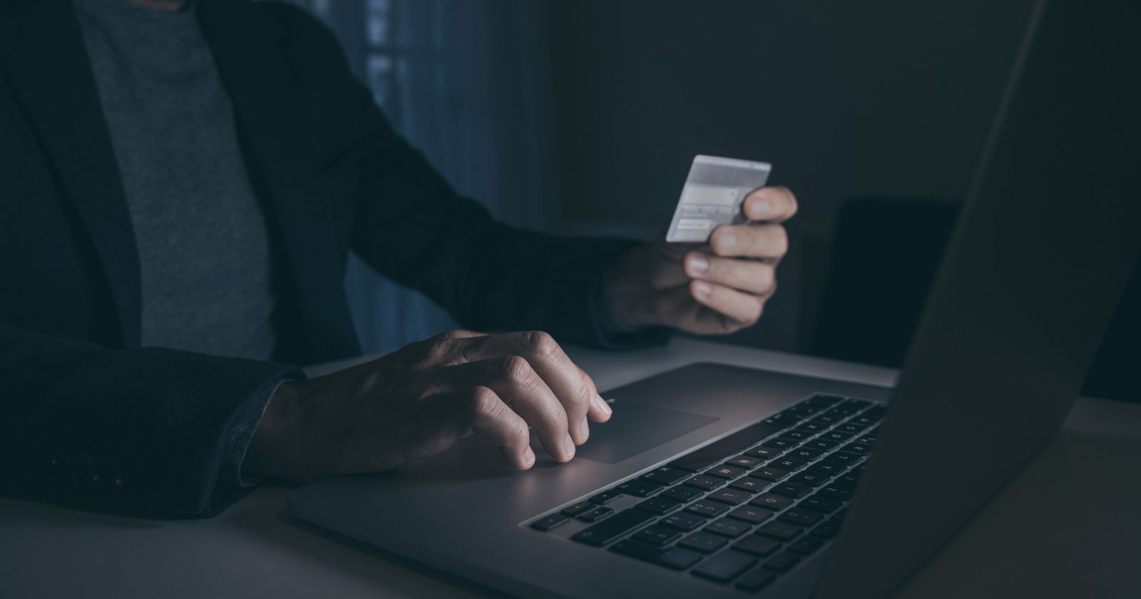 Person sitzt am Schreibtisch vor Laptop mit Karte in der Hand