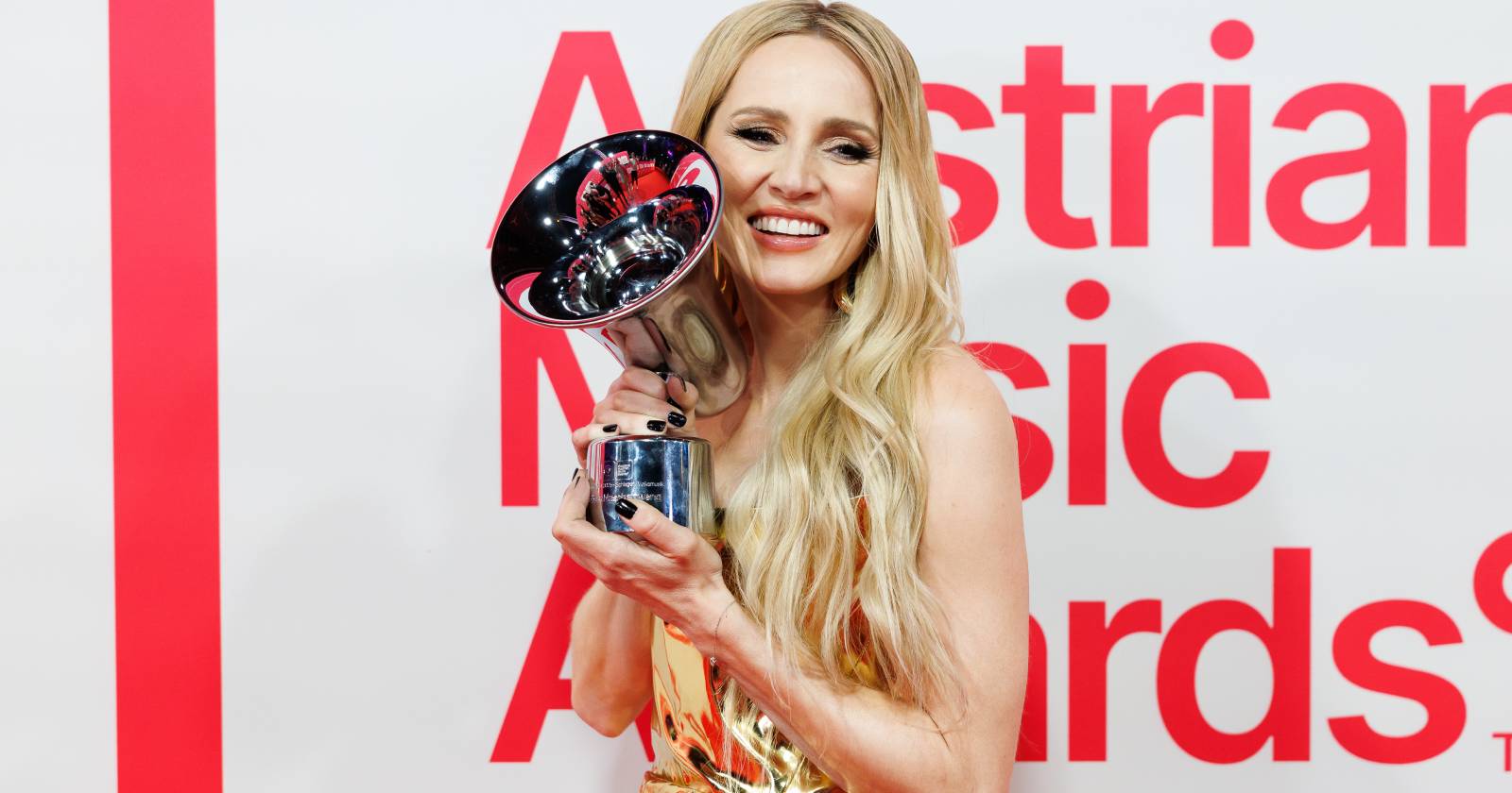 Melissa Naschenweng auf dem Roten Teppich des Amadeus Austrian Music Awards, die eine der Auszeichnungen mit zwei Händen neben ihr Gesicht hält