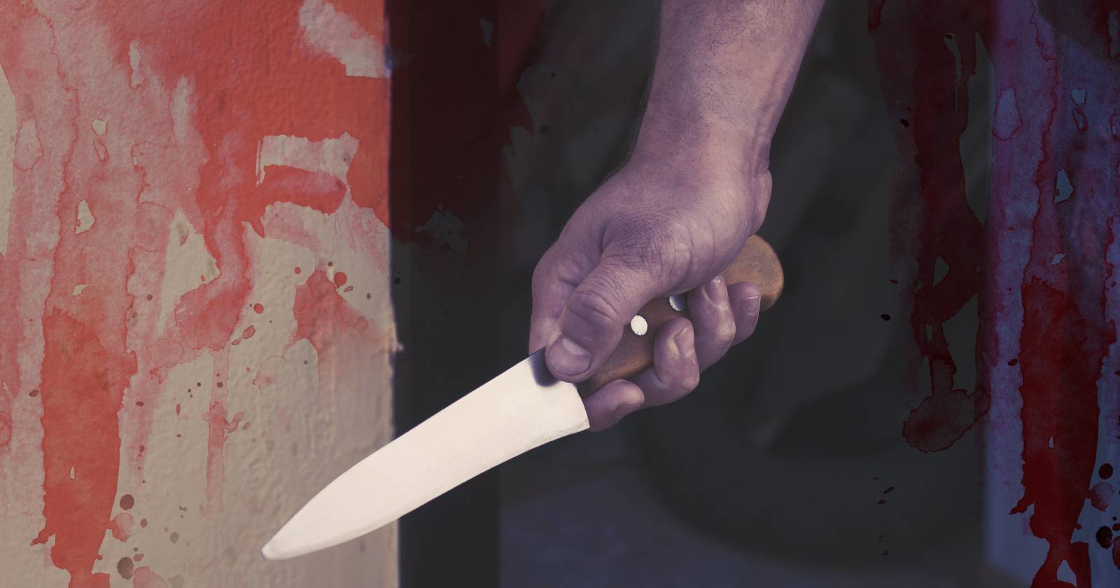 Nahaufnahme einer männlichen Hand, die ein Messer führt. Das Foto wurde mit künstlichen Blutflecken bedeckt.