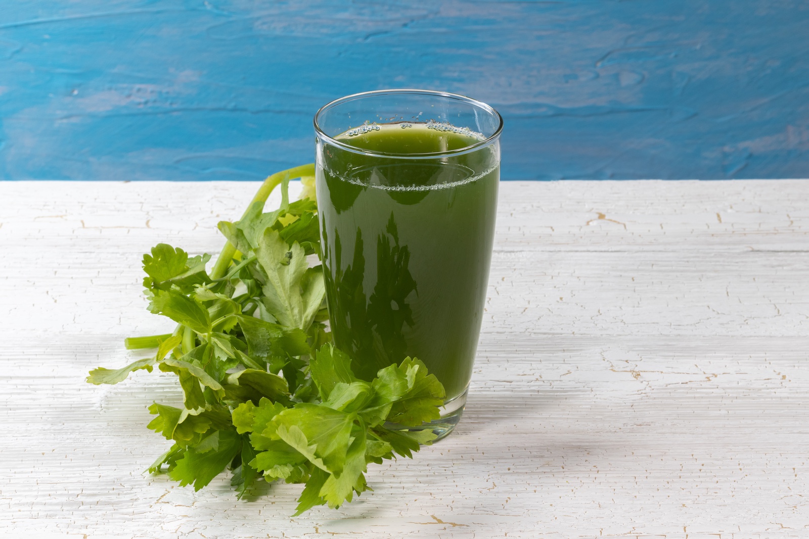 Ein Glas Sellerie-Saft, daneben ein Büschel Sellerie.