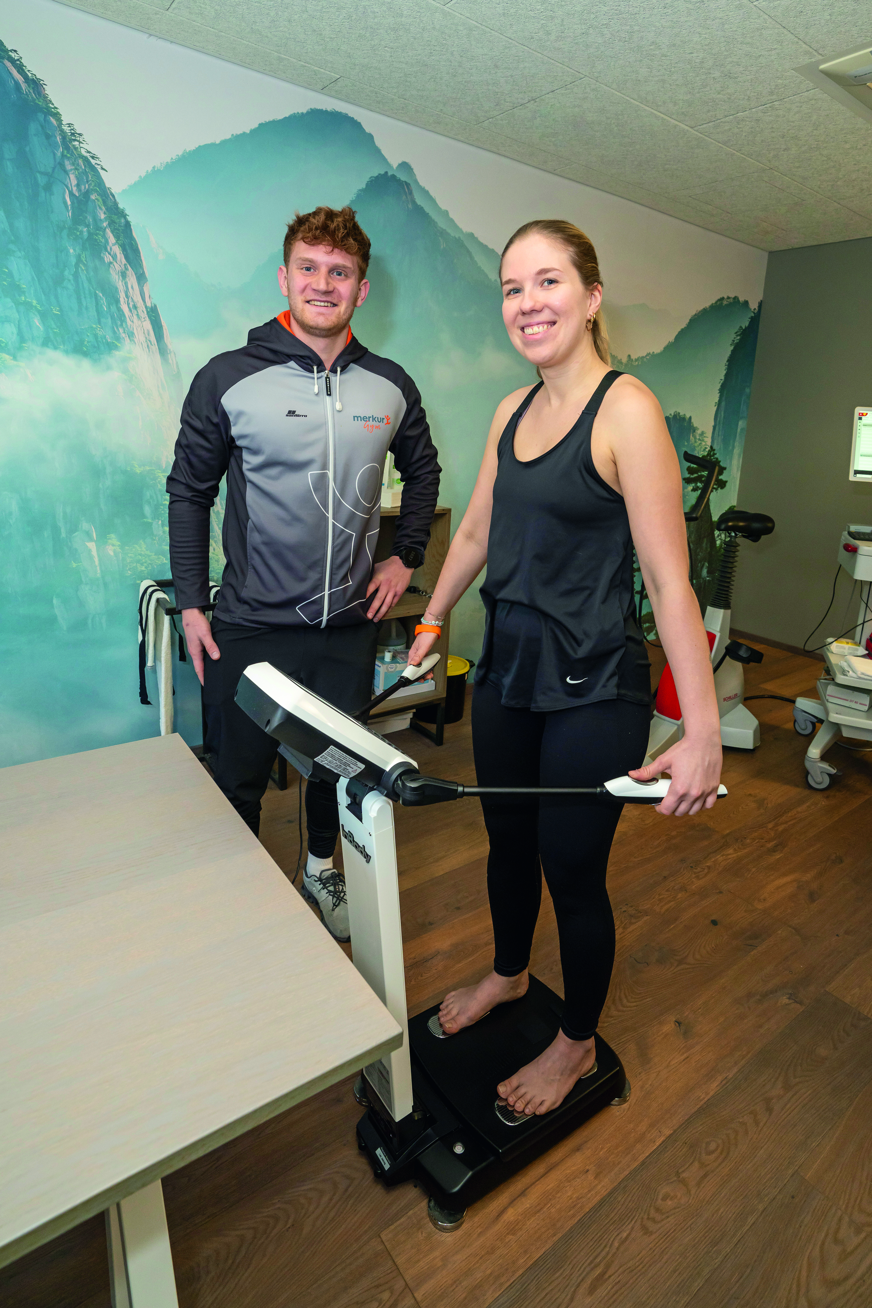Eine Frau steht auf einem Gerät, ein Trainer neben ihr