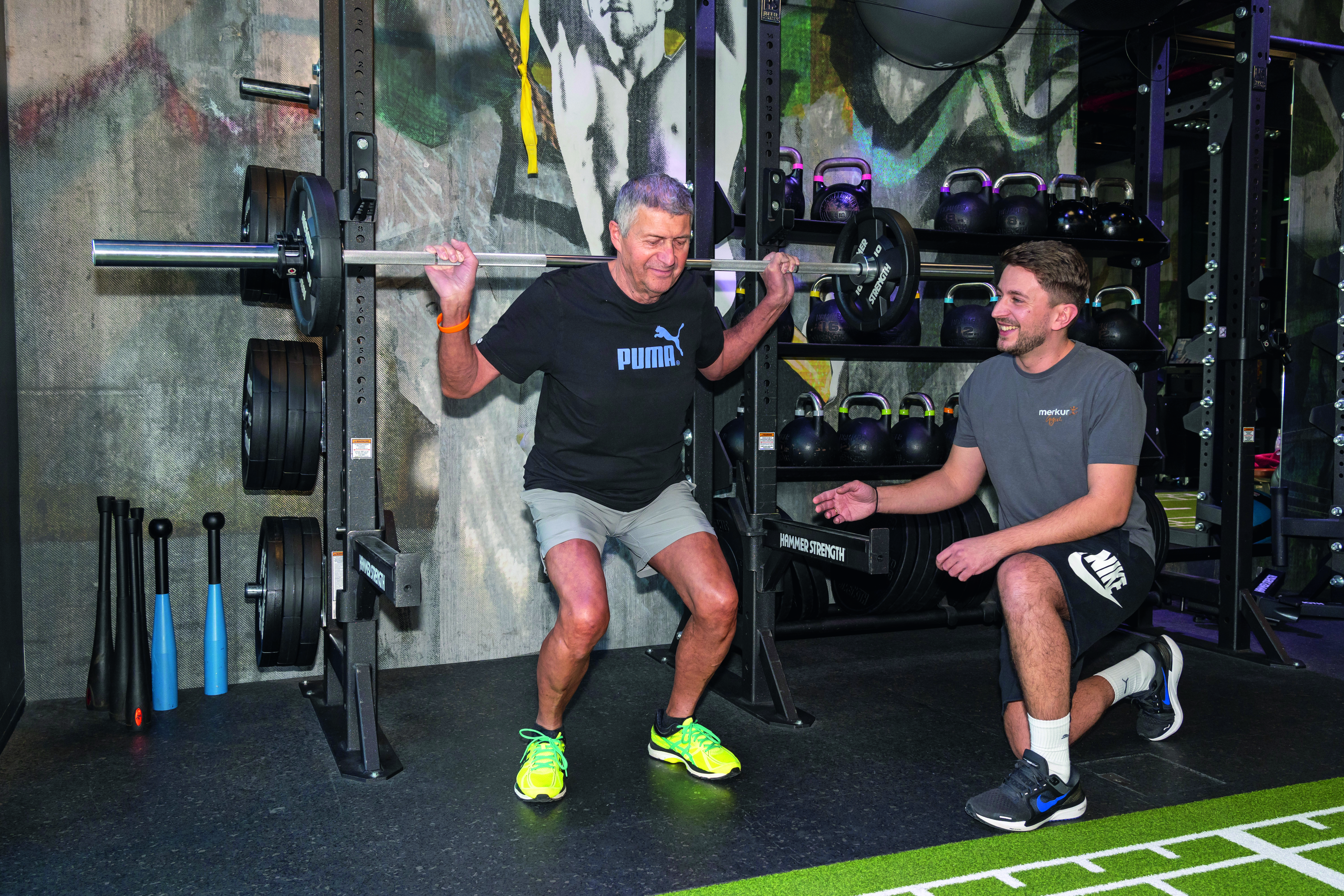 Ein Mann trainiert Gewichtsübungen, ein Trainer schaut zu