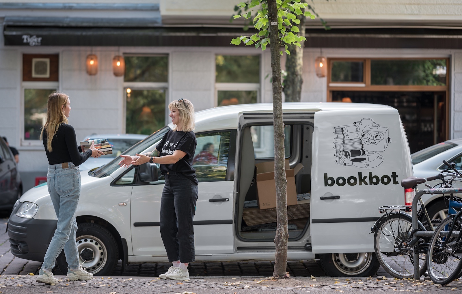 Zwei Frauen vor Lieferwagen übergeben Bücher