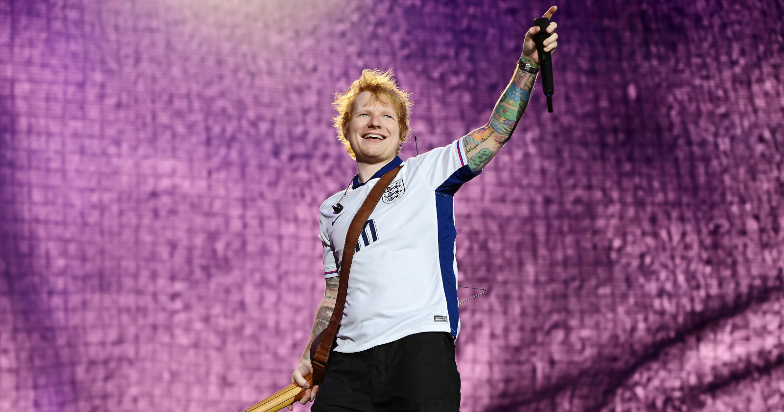 Sänger auf einer Bühne, in einer Hand hält er eine Gitarre