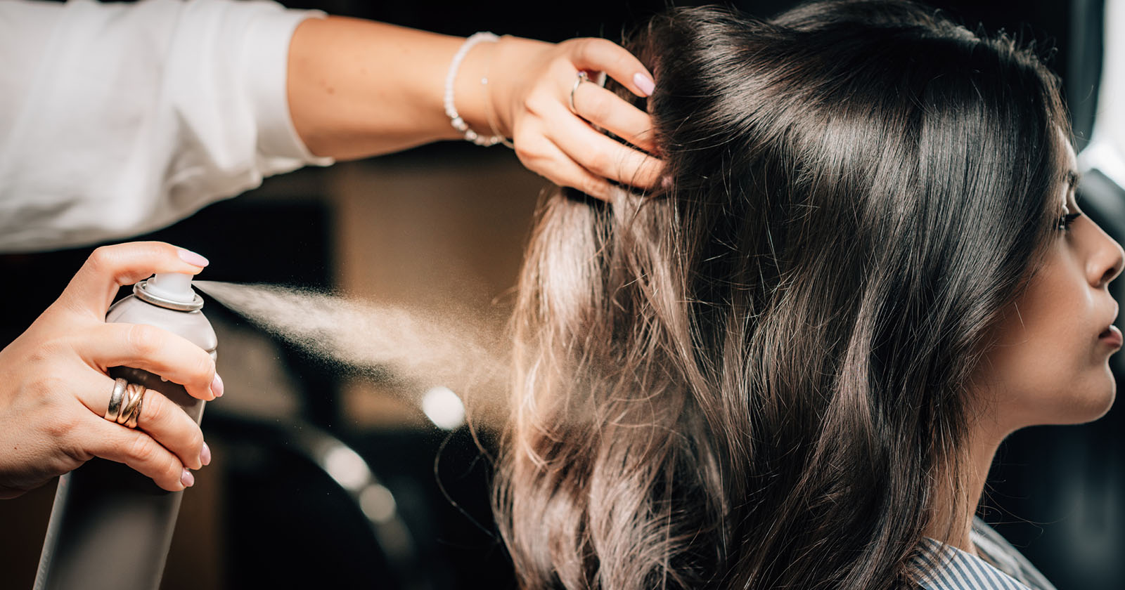 Frau sprüht Haarspray in Haare | Credit: iStock.com/microgen