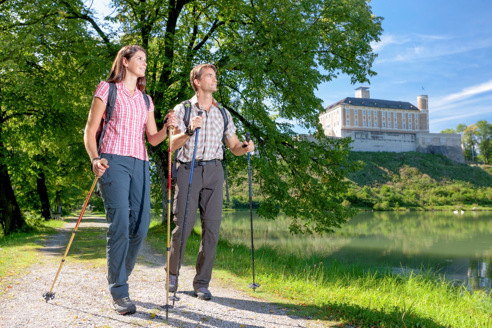 Eine Frau und ein Mann mit Walking Stöcken, im Hintergrund grüne Landschaft und das Schloss Trautenfeld.