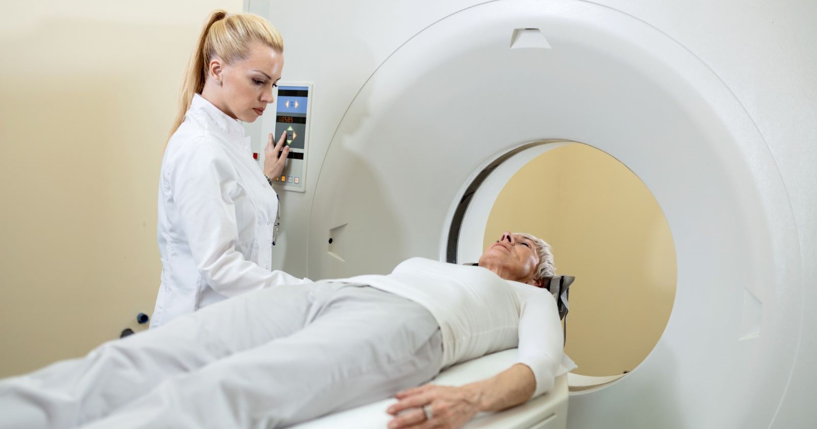 Eine Patientin liegt in einem MRT-Gerät, während eine medizinische Fachkraft das Gerät bedient – Symbolbild für künftig genehmigungspflichtige Untersuchungen.
