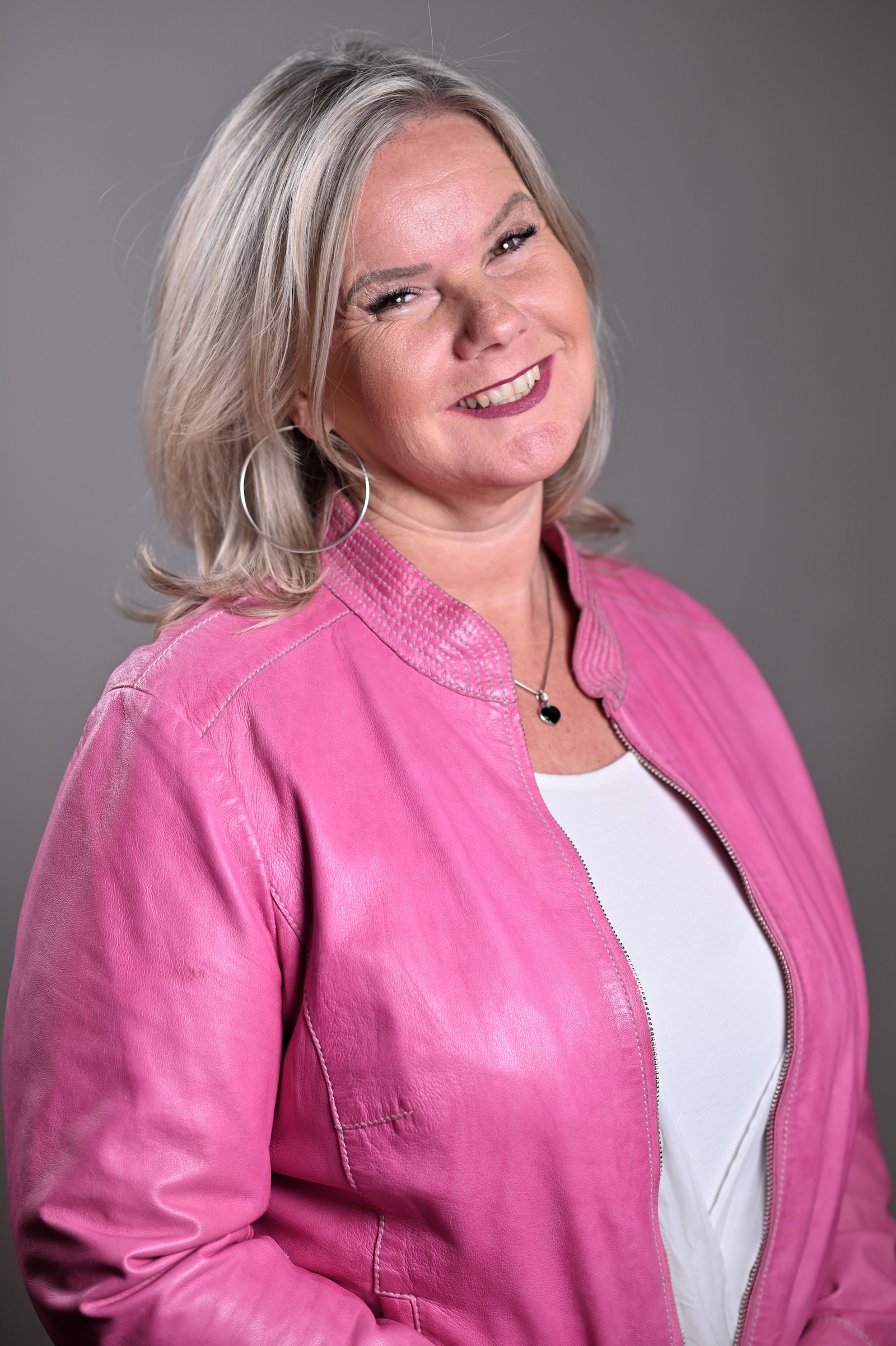 blonde Frau in einem weißen Shirt und einer pinken Jacke