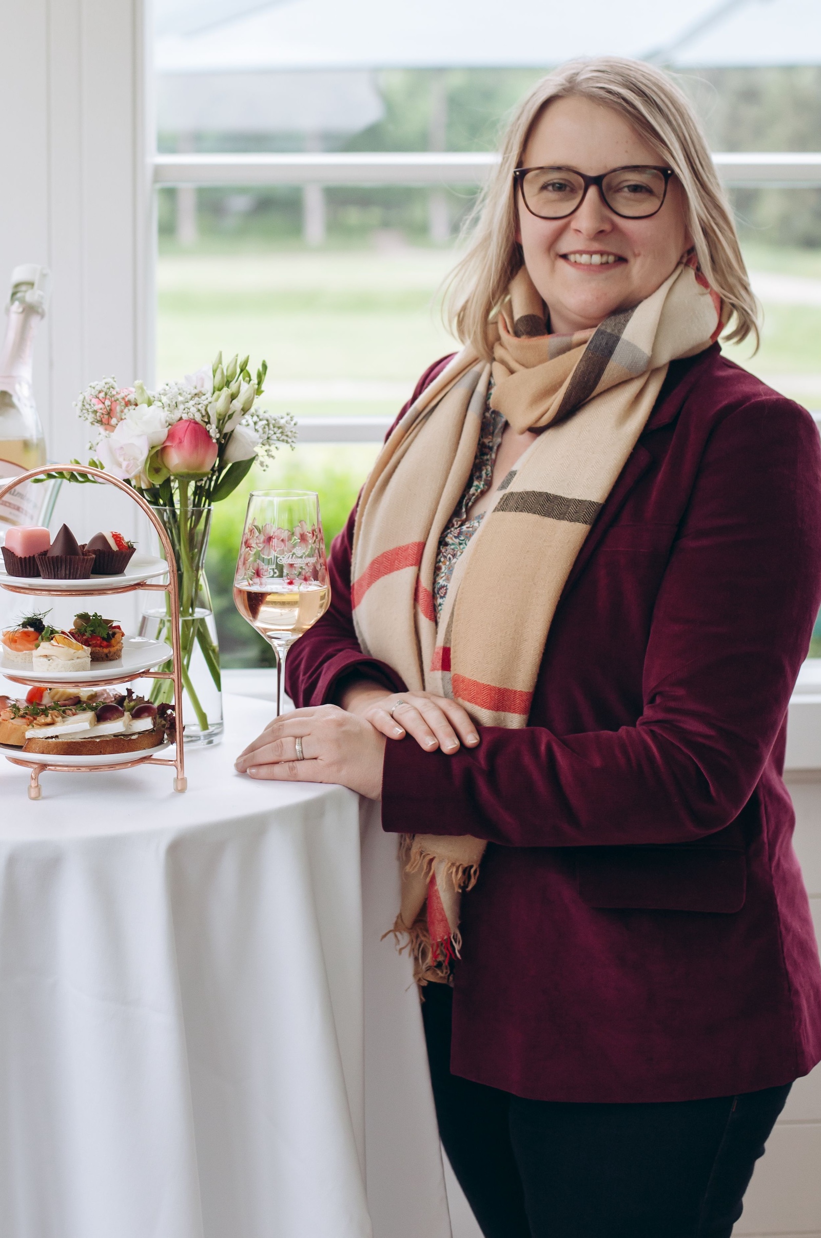 Frau mit weinrotem Blazer, Schal und einem Glas Sekt