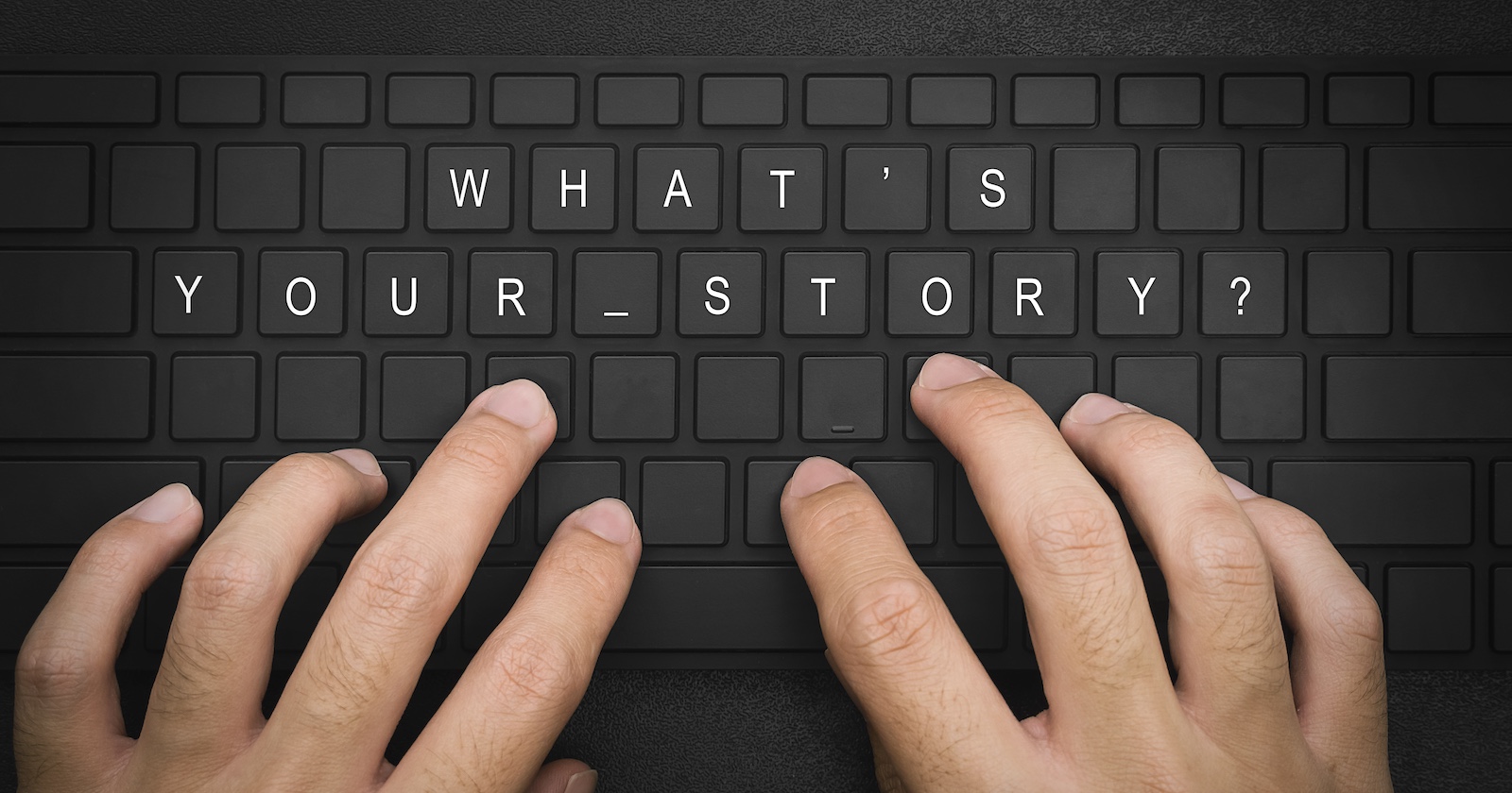 Zwei Hände tippen auf einer Tastatur, wo &quot;What's your Story?&quot; draufsteht.