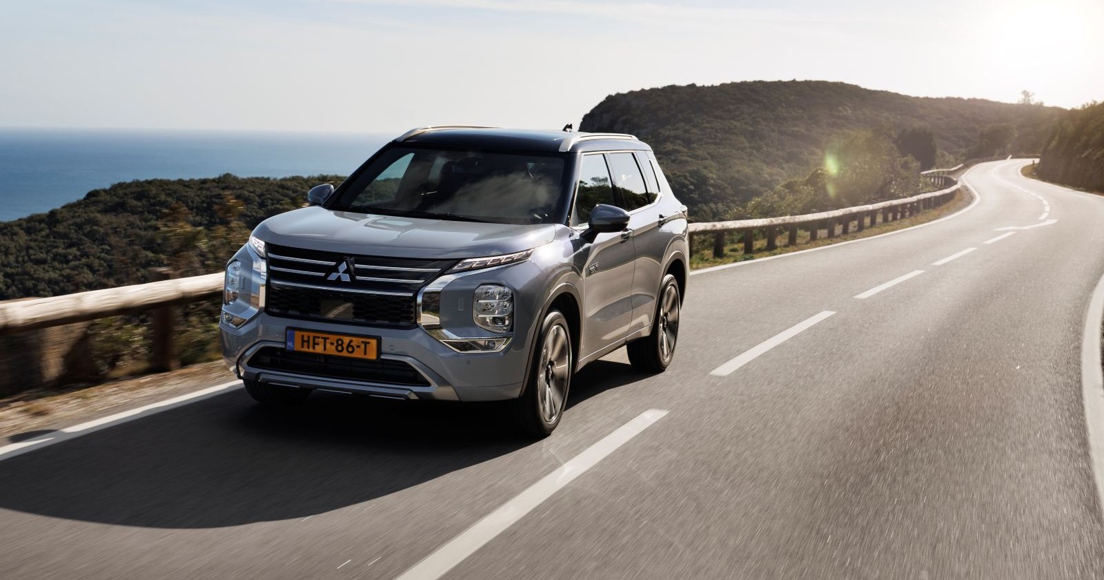 Ein silberner Mitsubishi Outlander fährt auf eine einsamen Landstraße. Im Hintergrund ist Macchie und das Meer zu sehen.
