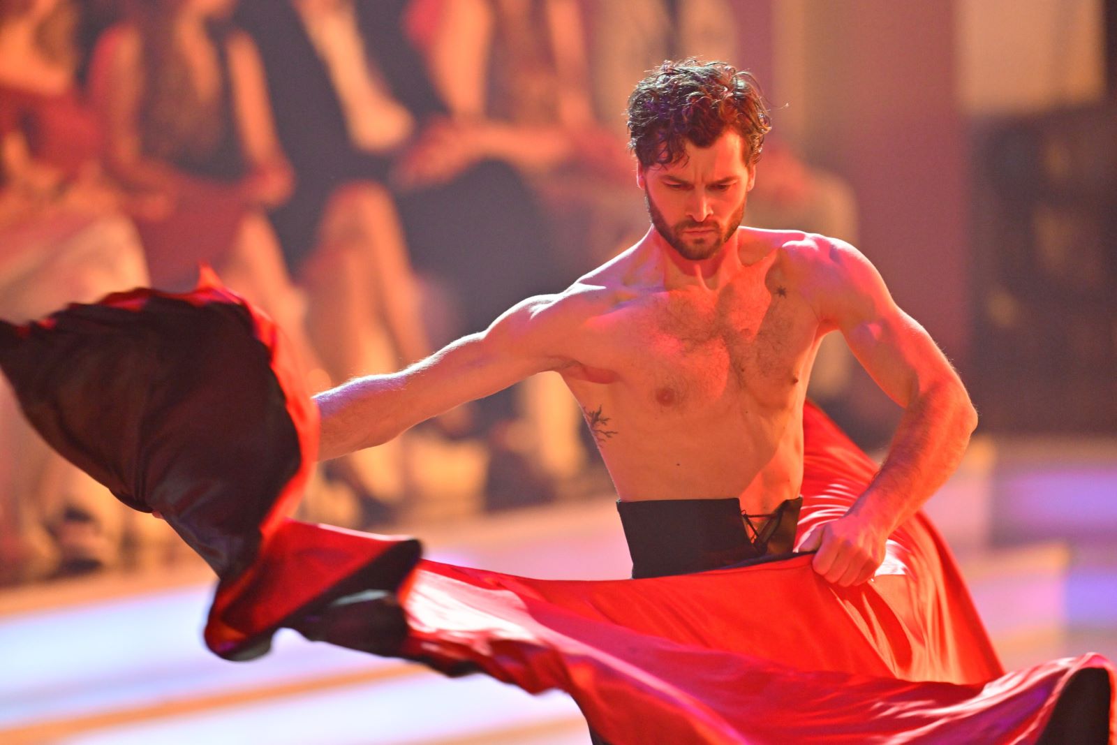 Aaron Karl tanzt im Finale von Dancing Stars 2025 oberkörperfrei einen Paso Doble. Er schwingt ein rotes Tuch mit Konzentration und Spannung, im Hintergrund verschwommene Zuschauer.