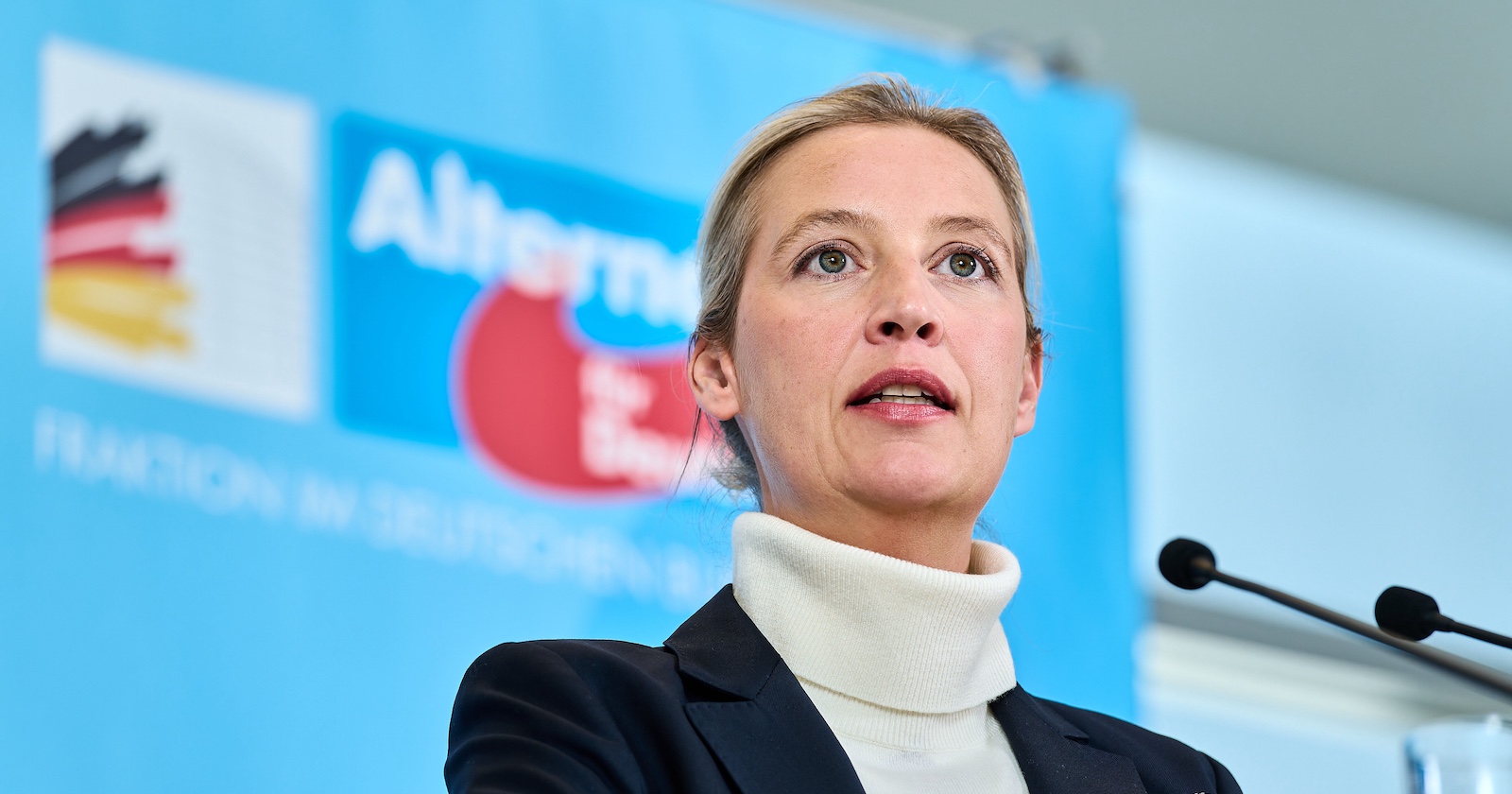 Alice Weidel, AfD-Bundesvorsitzende, spricht auf einer Pressekonferenz vor einem blauen Hintergrund mit AfD-Logo und Mikrofonen.