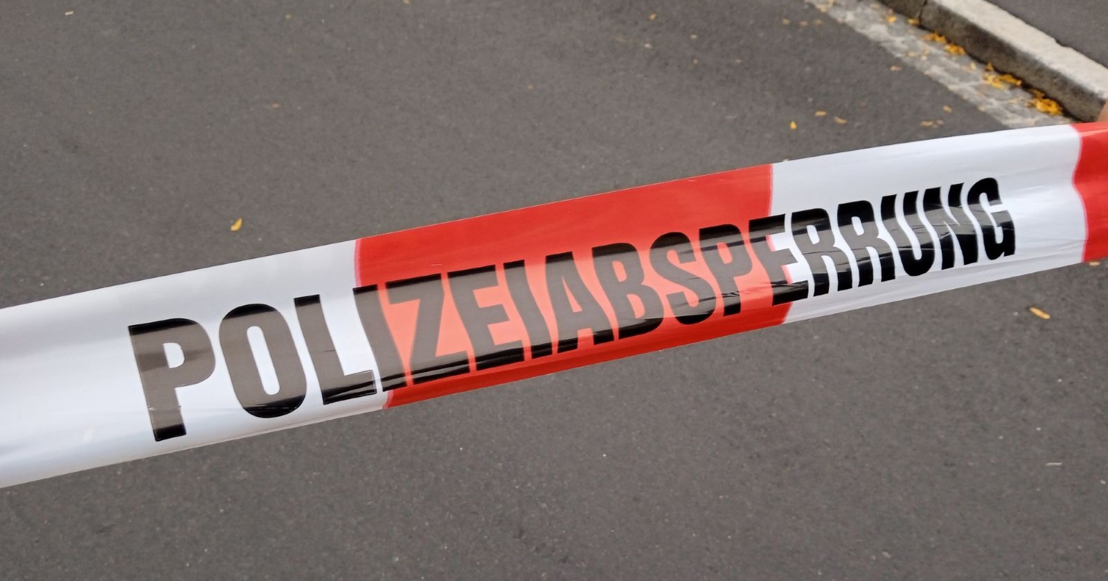 Polizeiabsperrband auf einer Straße angebrahct, auf dem Band steht in Blockbuchstaben das Wort POLIZEIABSPERRUNG geschrieben