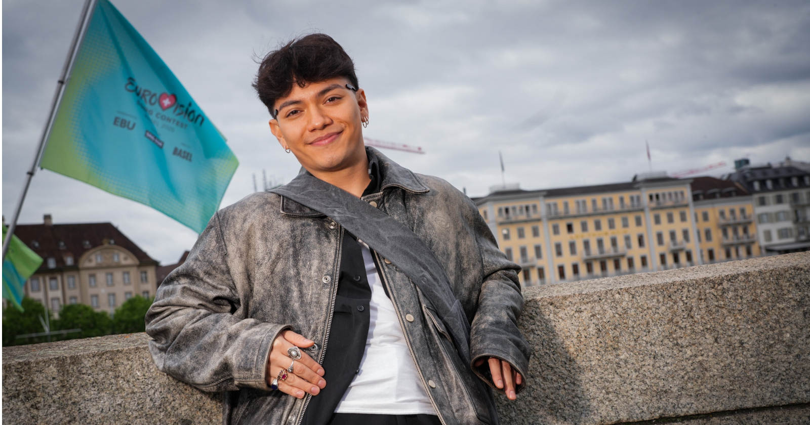 Mann lehnt an einer Mauer, hinter ihm weht eine Fahne