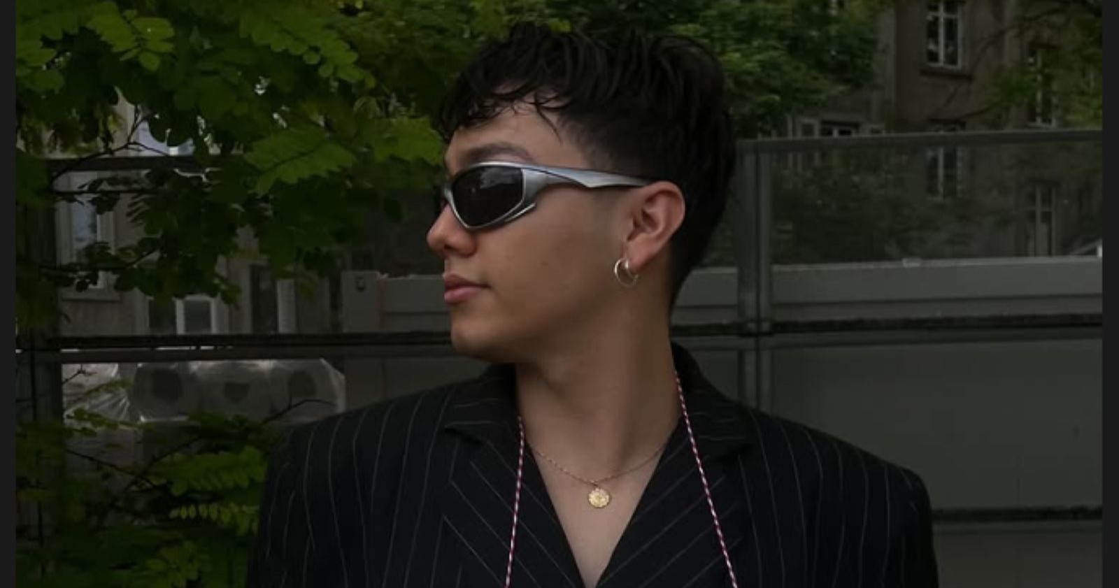 Johannes &quot;JJ&quot; Pietsch schaut zur Seite, trägt ein schwarzes Hemd, silberfarbene Ohrringe, eine goldfarbene Kette und eine Sonnenbrille