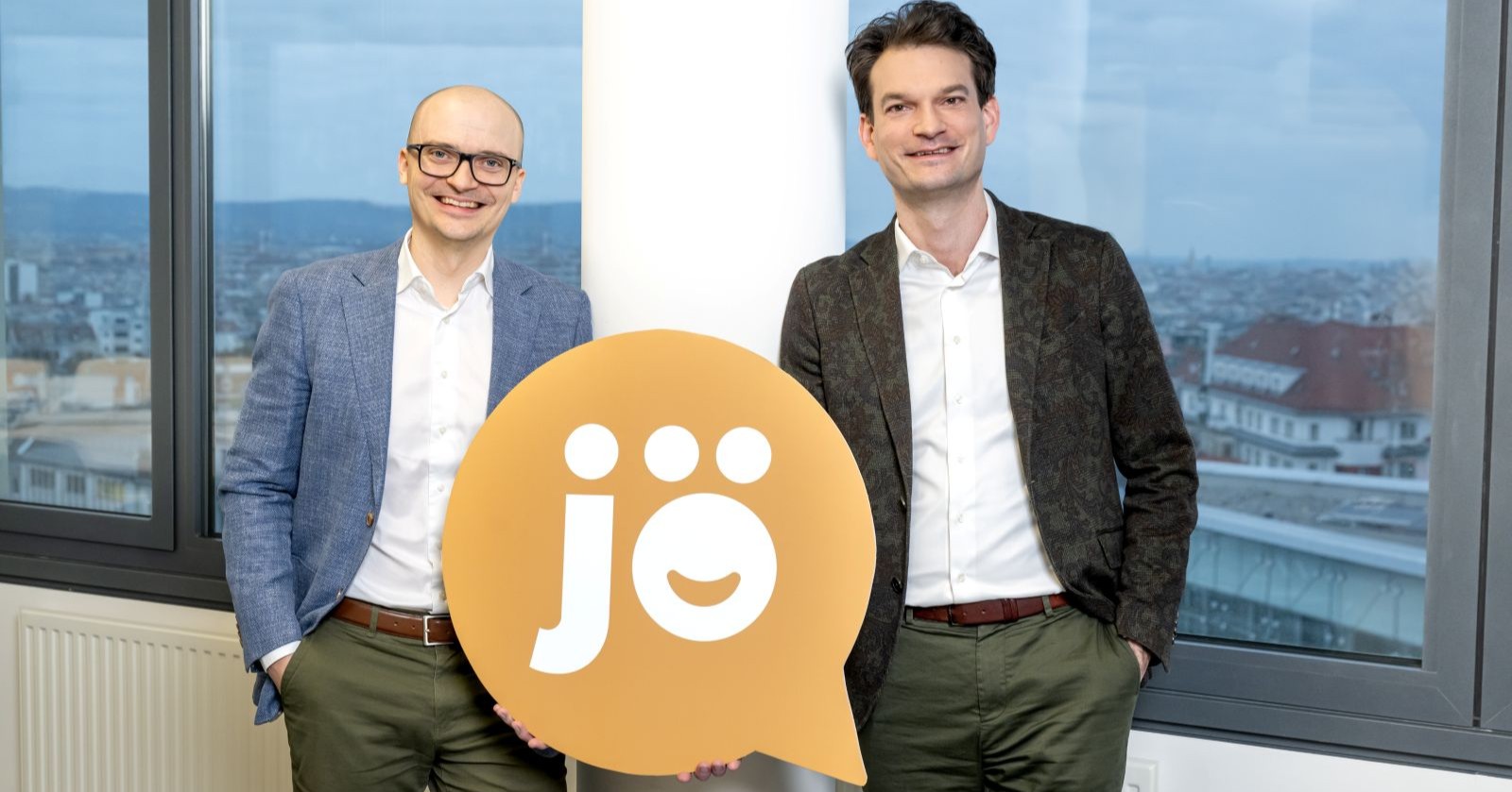 jö-Gescheftsführer Nikolai Scheurecker und Johannes Greller halten das jö-Logo: eine beigefarbene Sprechblase mit weißer, fetter Schrift &quot;jö&quot; innen