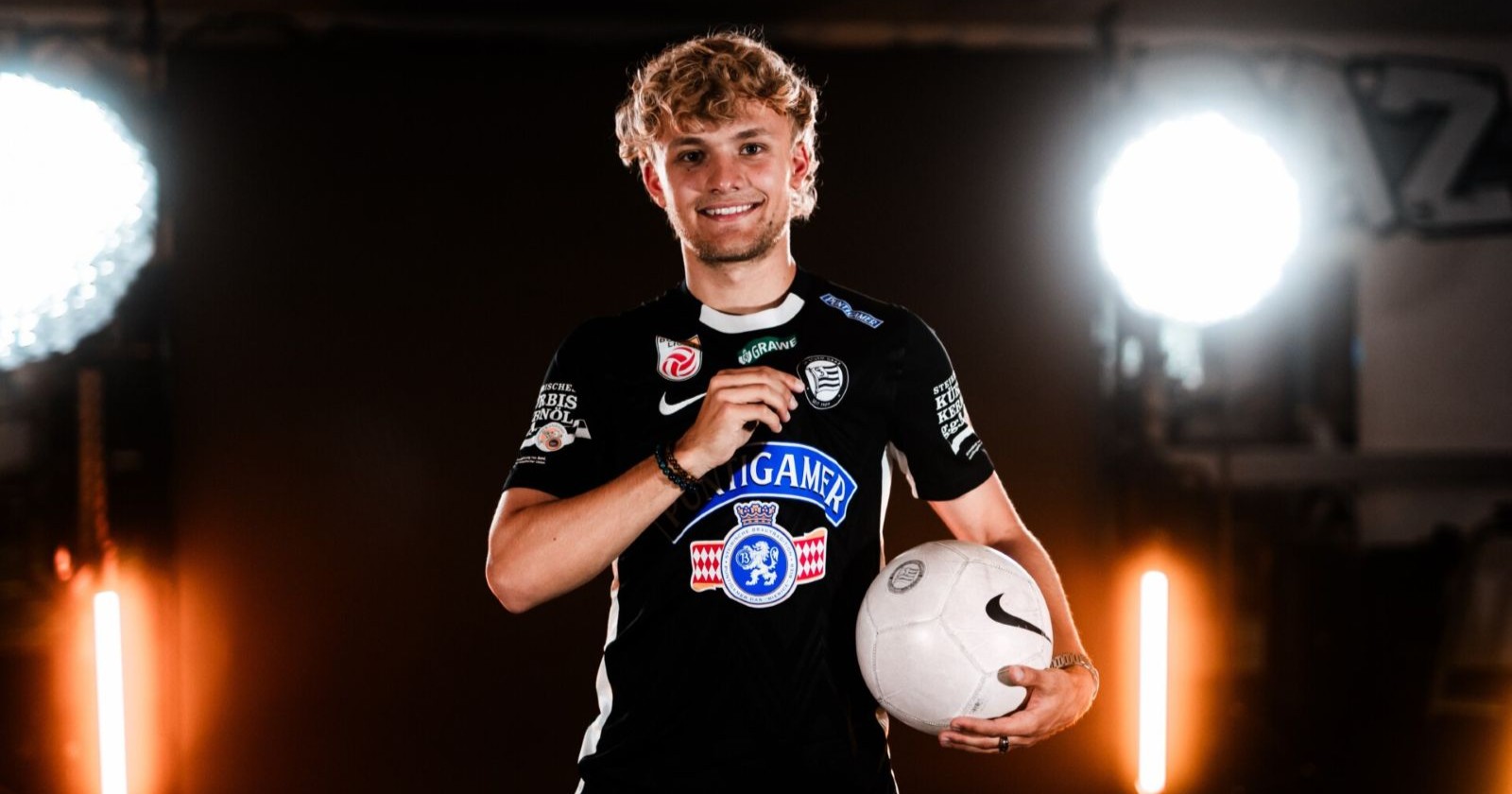 Julius Beck steht im Sturm Graz Trikot mit Ball in der Hand