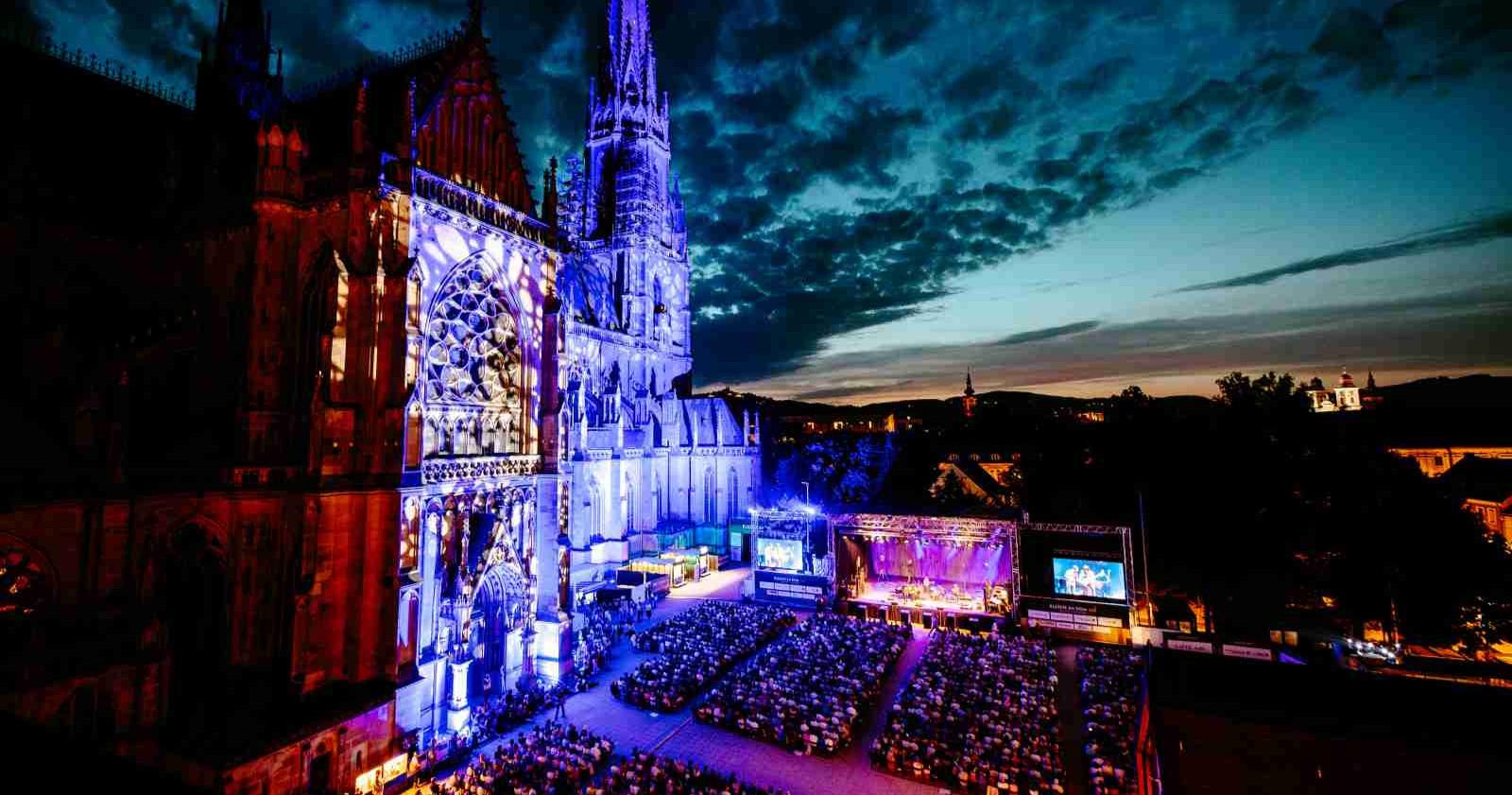 Klassik am Dom in Linz - beleuchteter Mariendom bei Nacht mit visuellen Effekten, großer Menschenmenge am Domplatz bei Open-Air-Konzert.