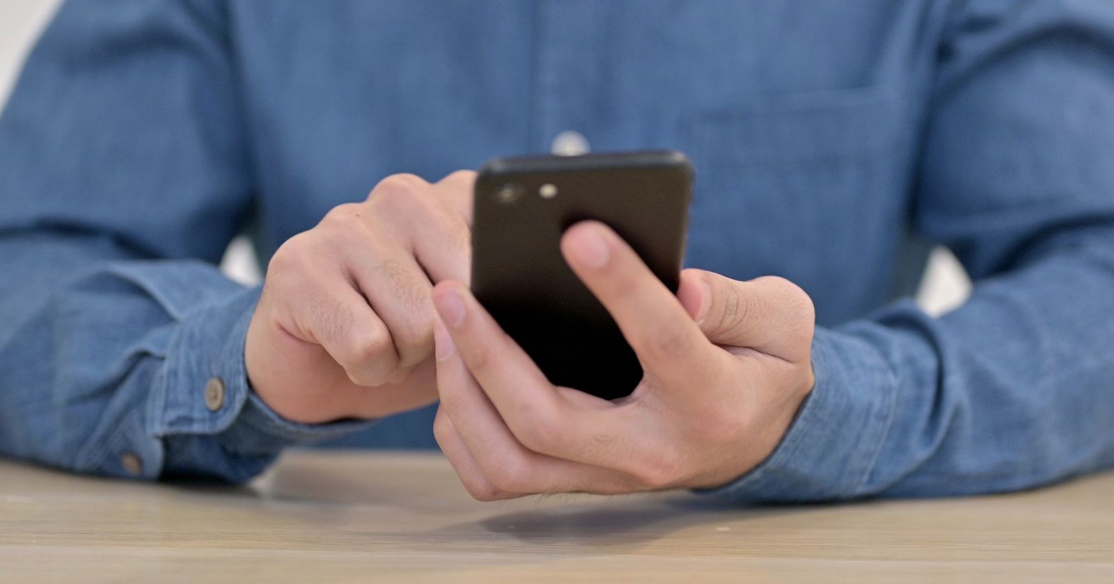 Nahaufnahme einer Person in Jeanshemd, die mit einem Smartphone in der Hand auf den Bildschirm tippt – kein Empfang erkennbar.