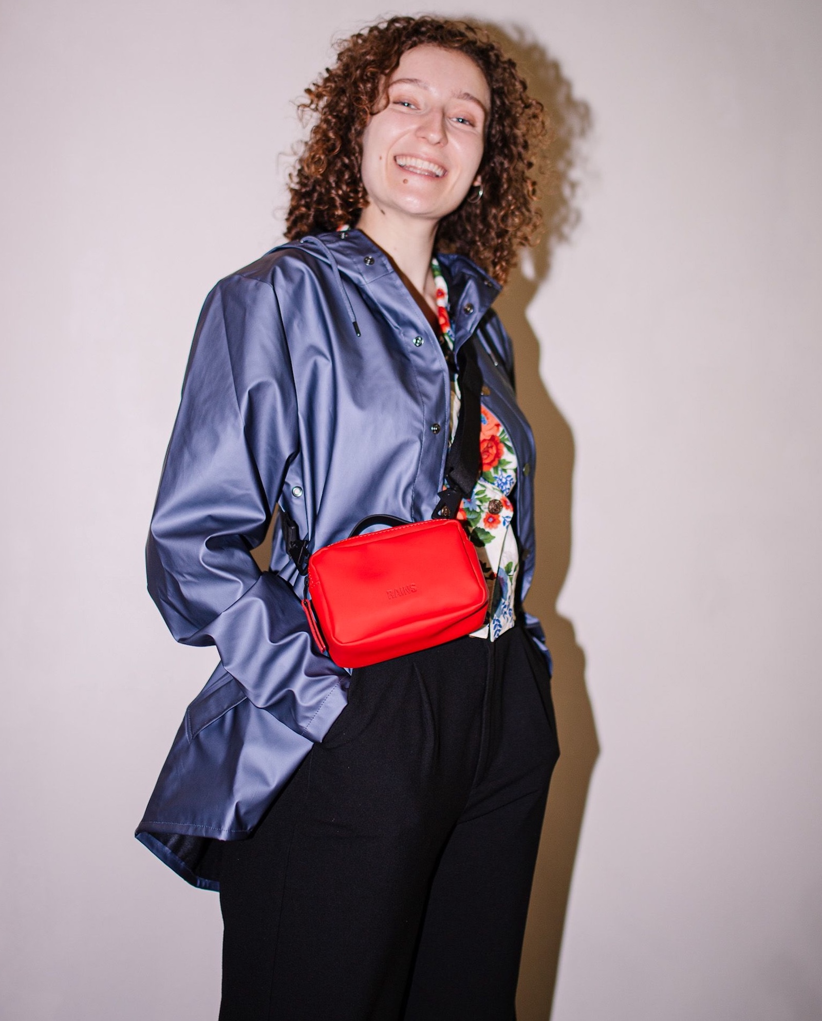 Frau mit schwarzen Hosen, violetter Jacke und roter Umhängetasche