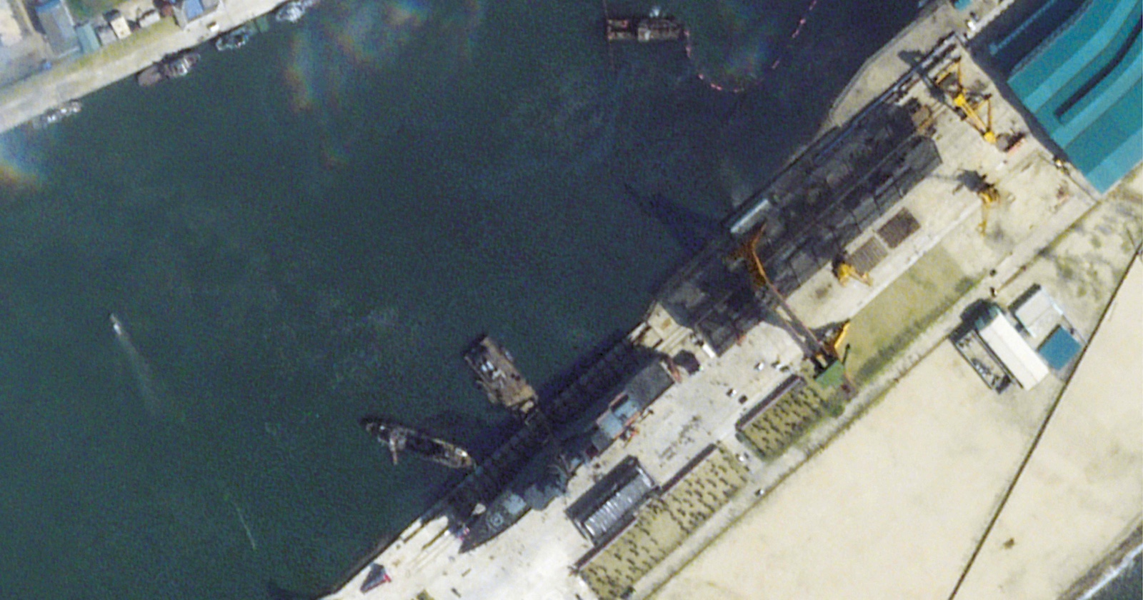 Satellitenbild eines nordkoreanischen Werftgeländes in Chongjin. Ein großes Kriegsschiff liegt seitlich im Wasser, umgeben von Kränen und Werftbauten entlang der Kaimauer.